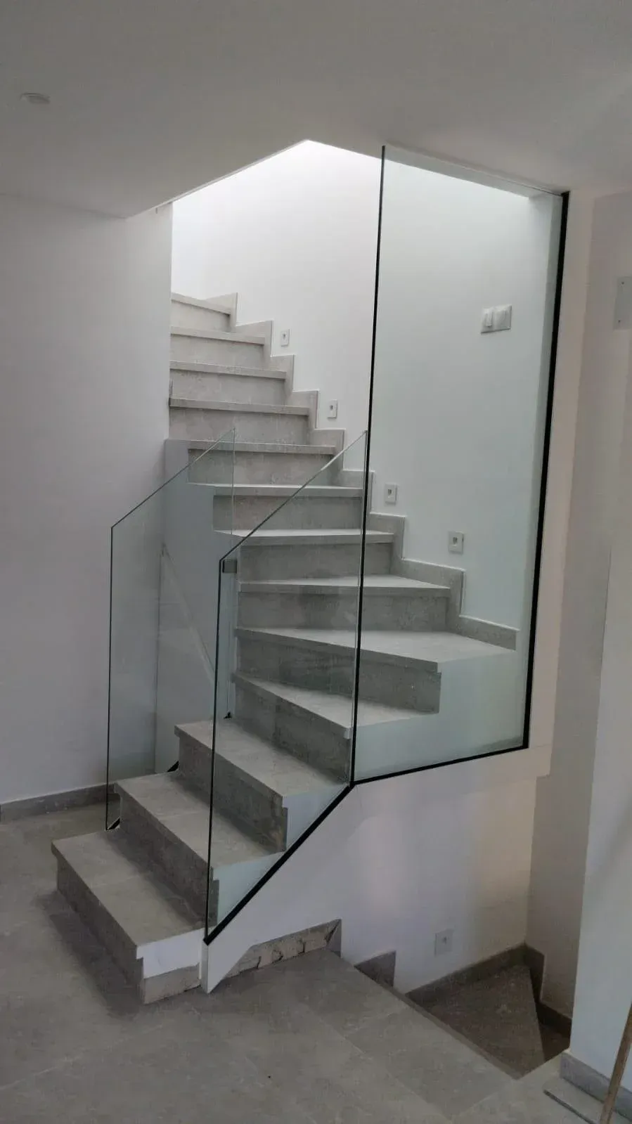 Una escalera de piedra de color claro con un sistema de barandilla de cristal moderno y minimalista, situada en un interior contemporáneo.