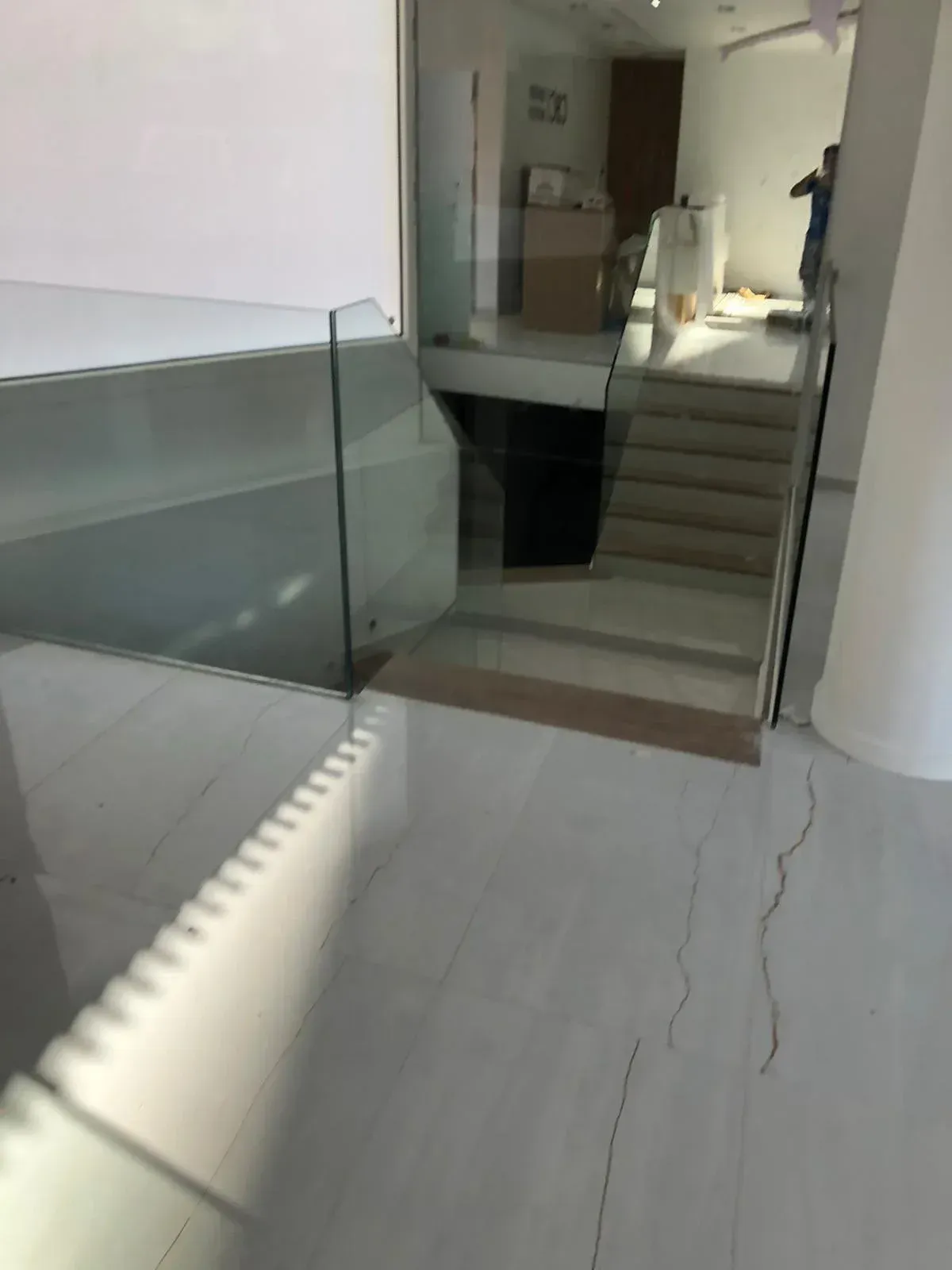 Vista de un interior moderno con suelo blanco, barandilla de cristal y escalera que conduce a la planta superior.