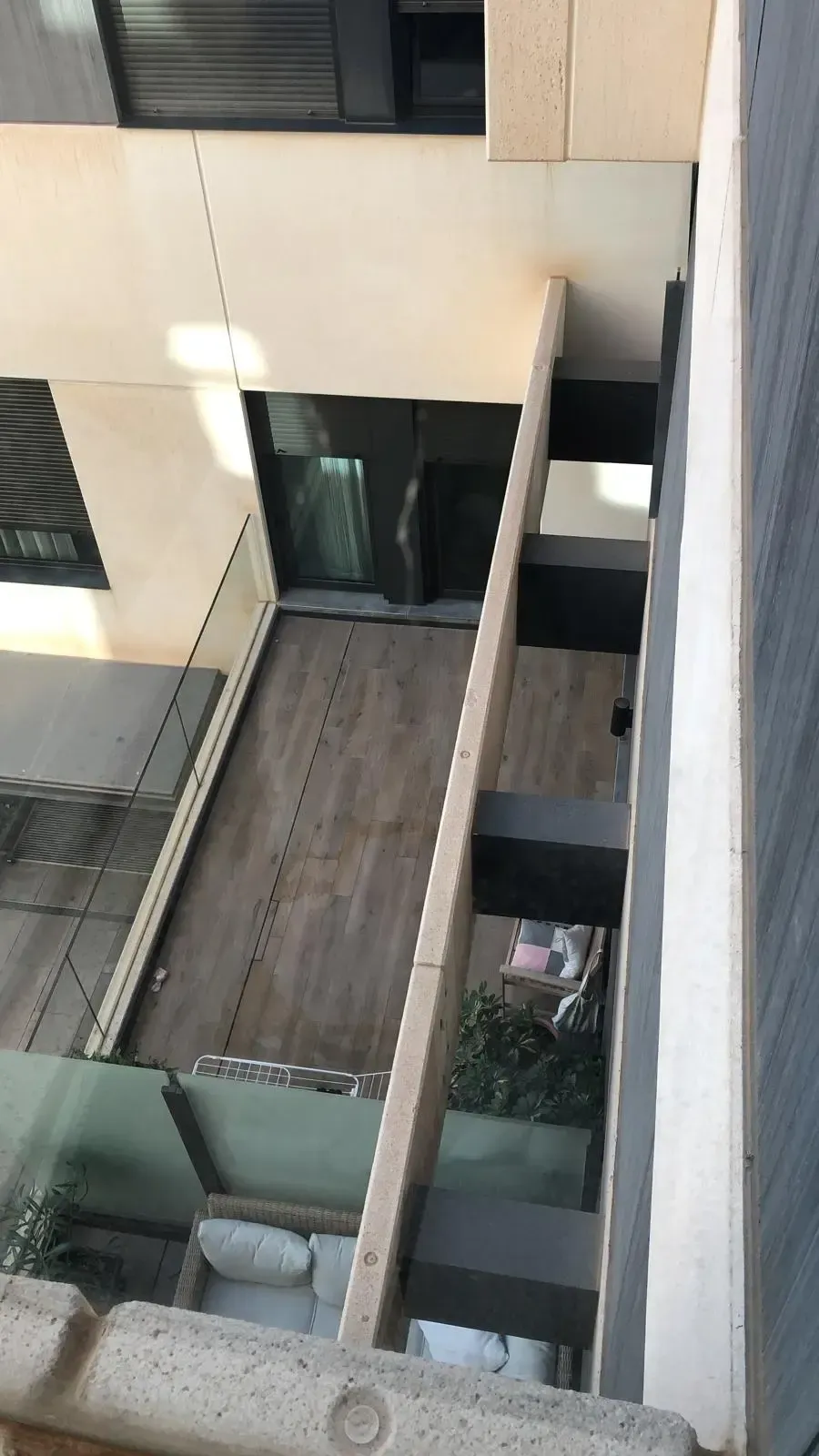 Vista desde un ángulo elevado del balcón de un apartamento moderno con suelo de madera, vigas estructurales oscuras y asientos al aire libre.