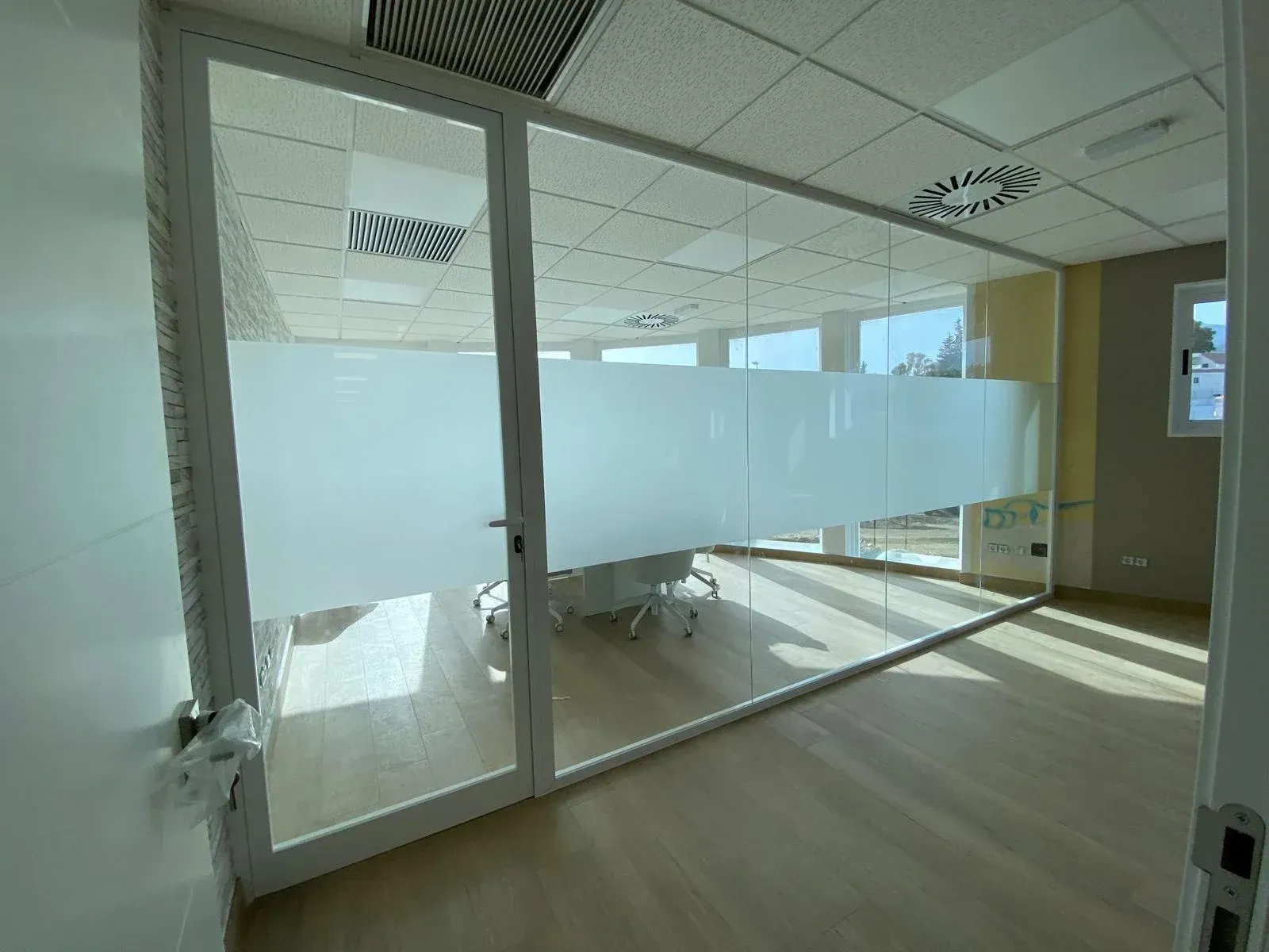 Interior de oficina moderno con sala de conferencias con paredes de cristal, franjas de privacidad esmeriladas y suelo de madera clara.