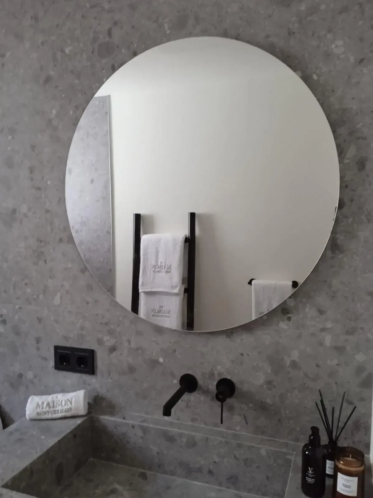 En un baño moderno y minimalista, un espejo redondo cuelga sobre un tocador de piedra gris con grifería negra mate.