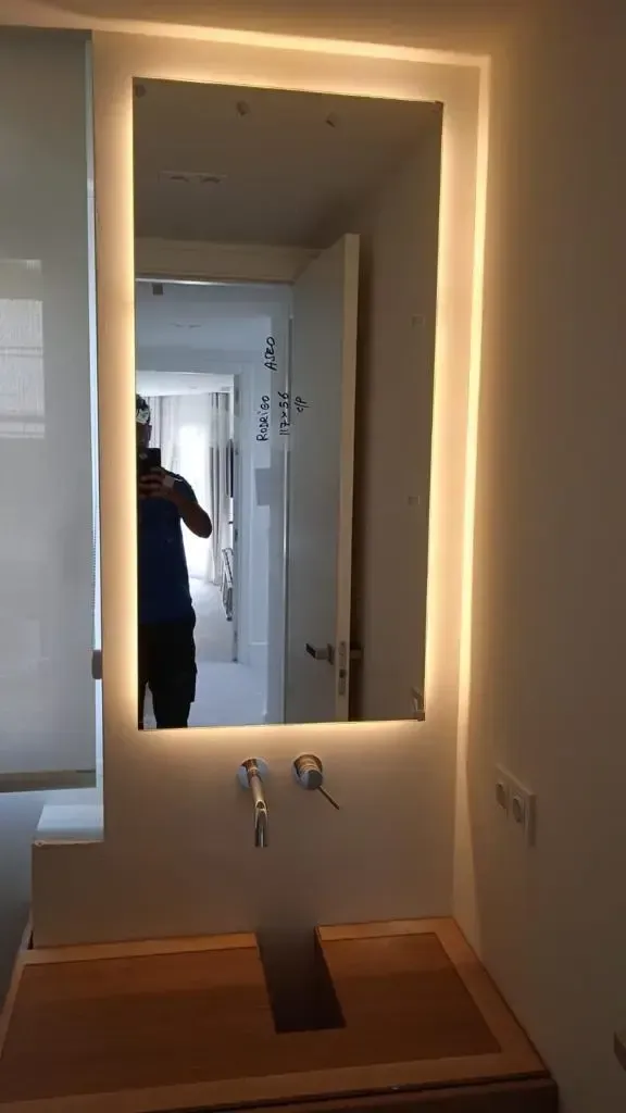 Un mueble de baño con espejo de pared rectangular iluminado, un elegante grifo plateado y una encimera minimalista de piedra para el lavabo.