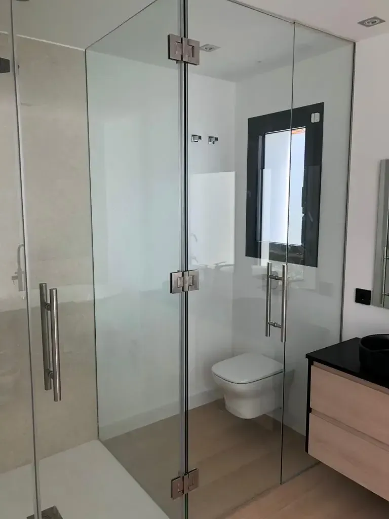 Un baño moderno cuenta con una cabina de ducha con mampara de cristal junto a un inodoro suspendido y un tocador con encimera negra.