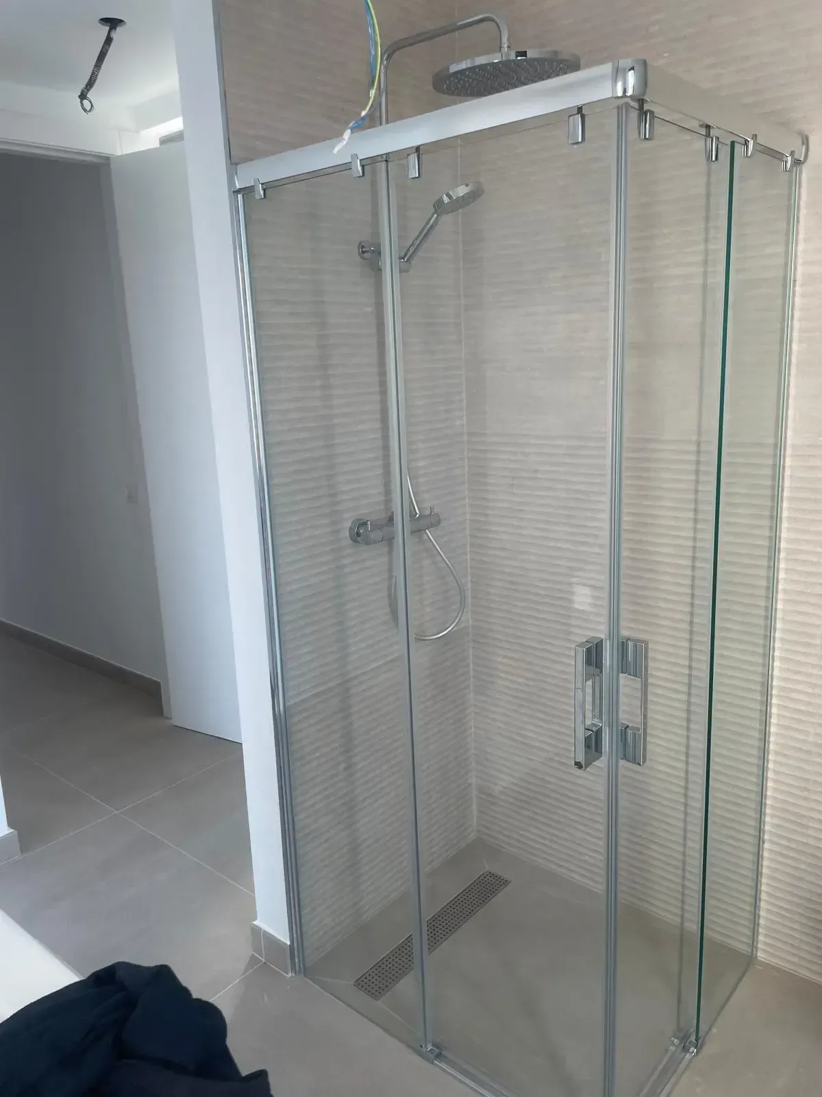 Una cabina de ducha cuadrada de cristal con marcos cromados, un cabezal de ducha tipo lluvia y una alcachofa de mano, todo ello en un baño alicatado.