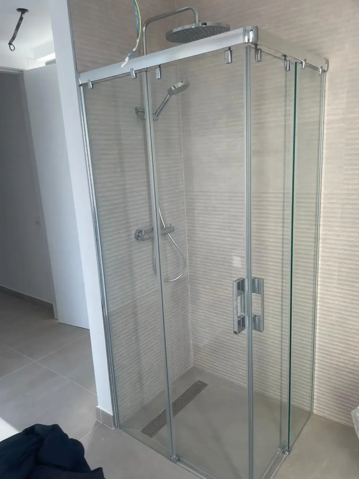 Una cabina de ducha cuadrada, cerrada con cristal, con marco cromado, cabezal de ducha tipo lluvia, rociador de mano y paredes alicatadas.