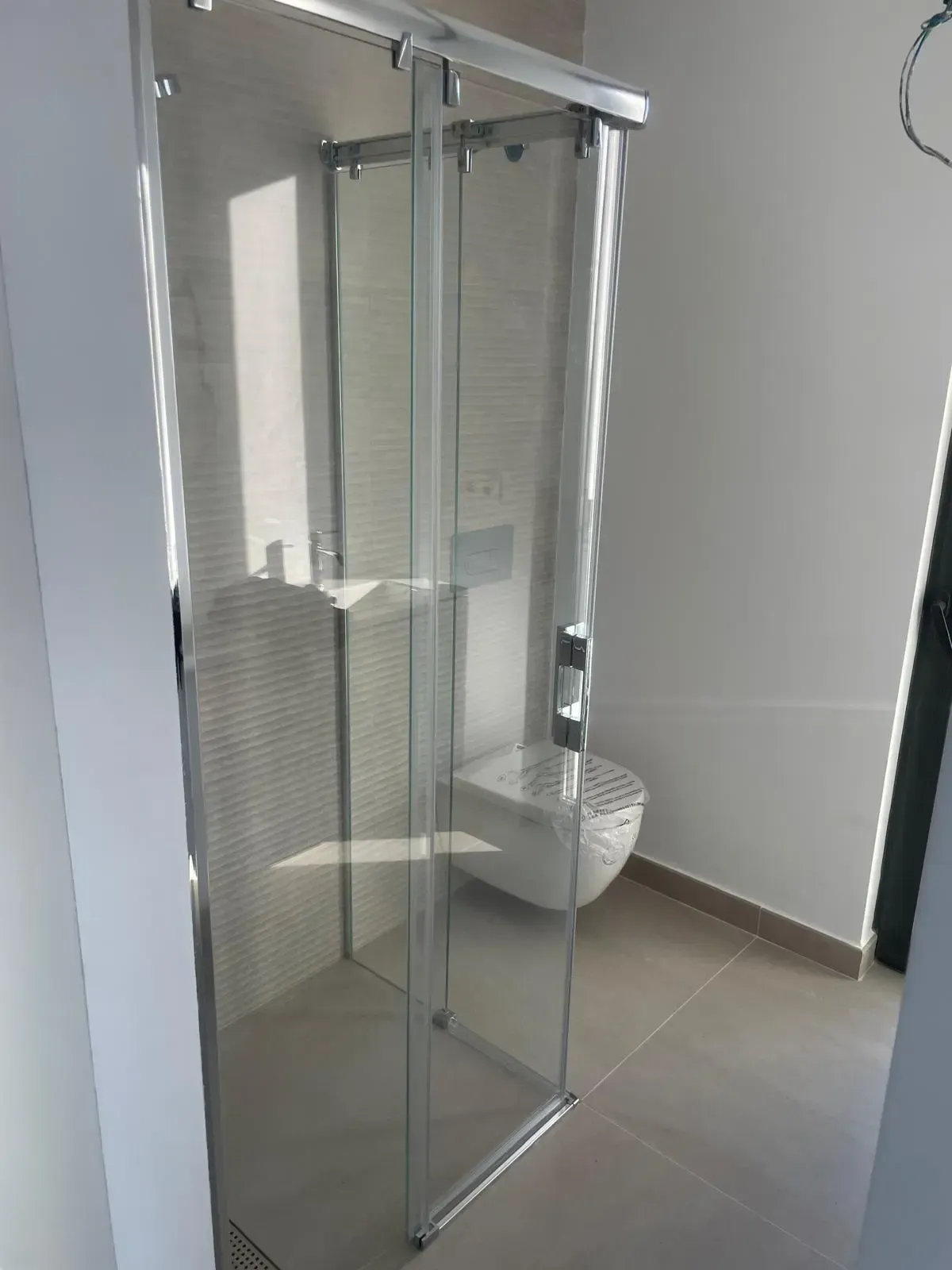 Una moderna mampara de ducha de cristal instalada en un baño con paredes alicatadas en color beige y suelo de baldosas de color claro.