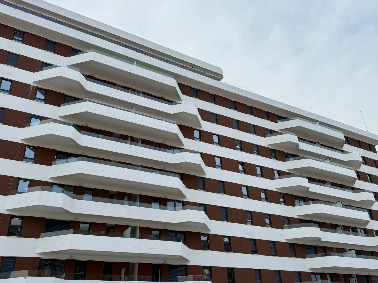 Un moderno edificio de apartamentos con balcones ondulados de color blanco que contrastan con una fachada marrón y blanca.