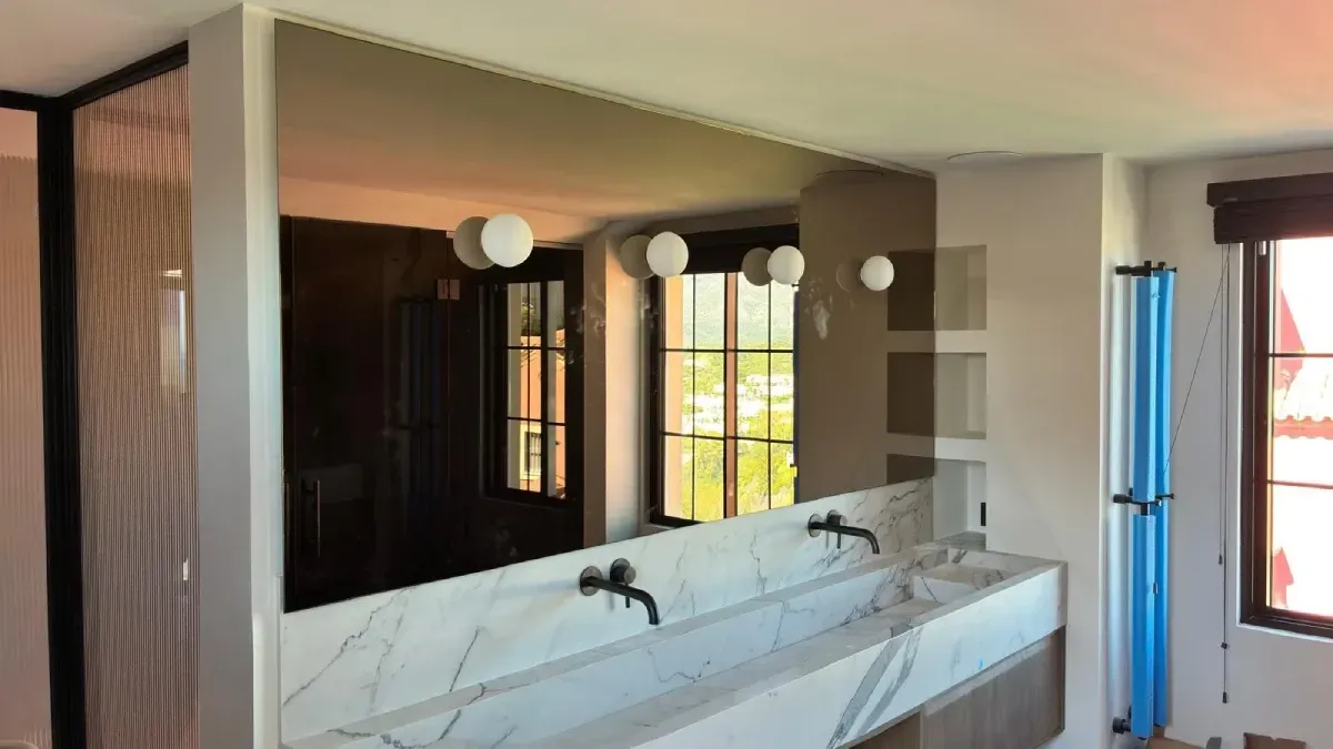 moderno tocador de baño con un gran espejo rectangular retroiluminado y grifos dobles.