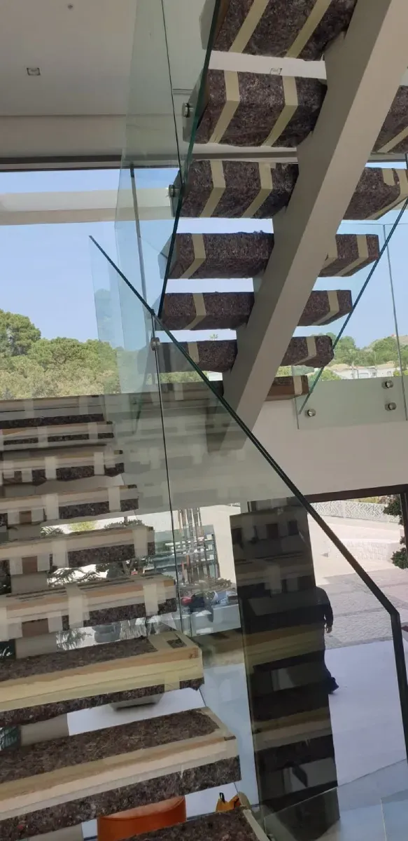 Una escalera con barandilla de vidrio, vista desde un ángulo que permite apreciar tanto el nivel superior como el inferior.