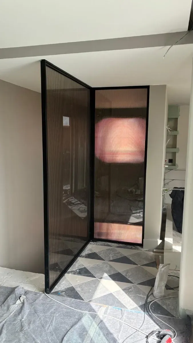 Una moderna mampara de cristal con marco metálico separa una entrada con azulejos geométricos de una habitación.