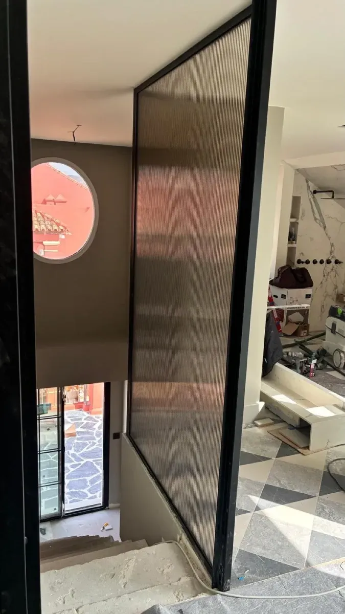 Vista de una escalera con una mampara alta de marco negro con un patrón de vidrio texturizado y ondulado.