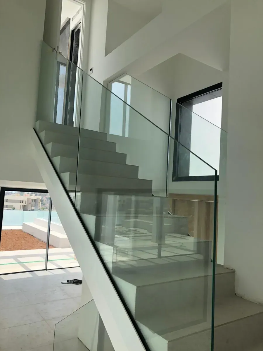 Escalera moderna de color blanco con diseño minimalista y barandilla de cristal transparente, iluminada por luz natural.