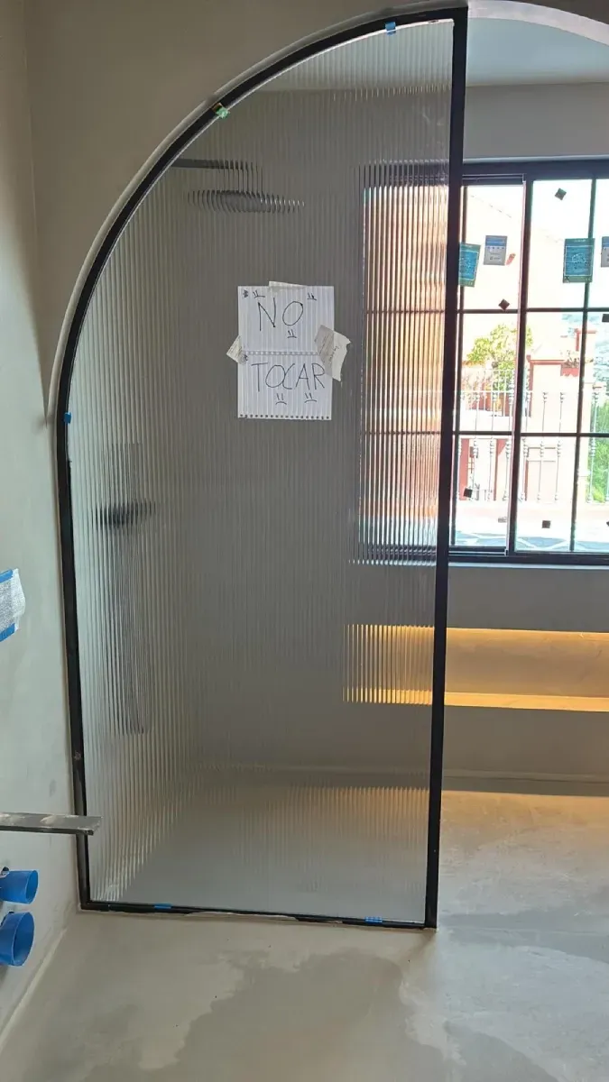 Una mosquitera plisada y retráctil instalada en un marco arqueado semicircular dentro de una habitación.