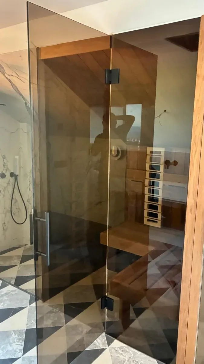 Una puerta de cristal con bisagras y manija negras da acceso a una sauna