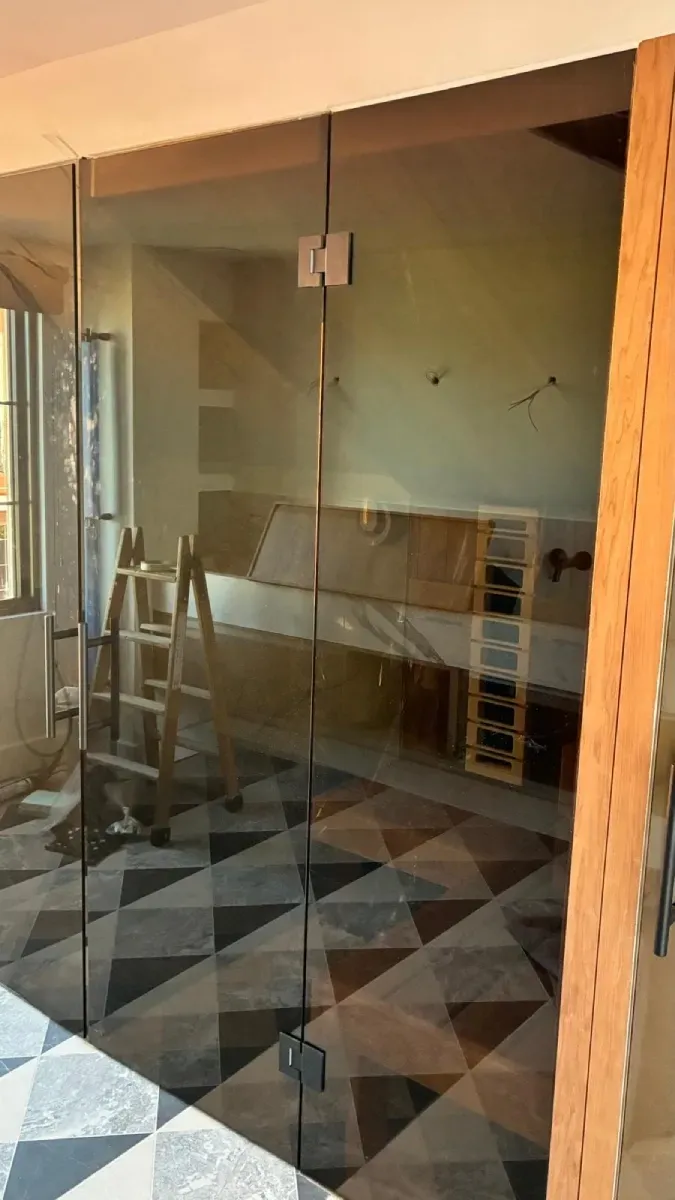 Una mampara de cristal con bisagras y tirador metálicos