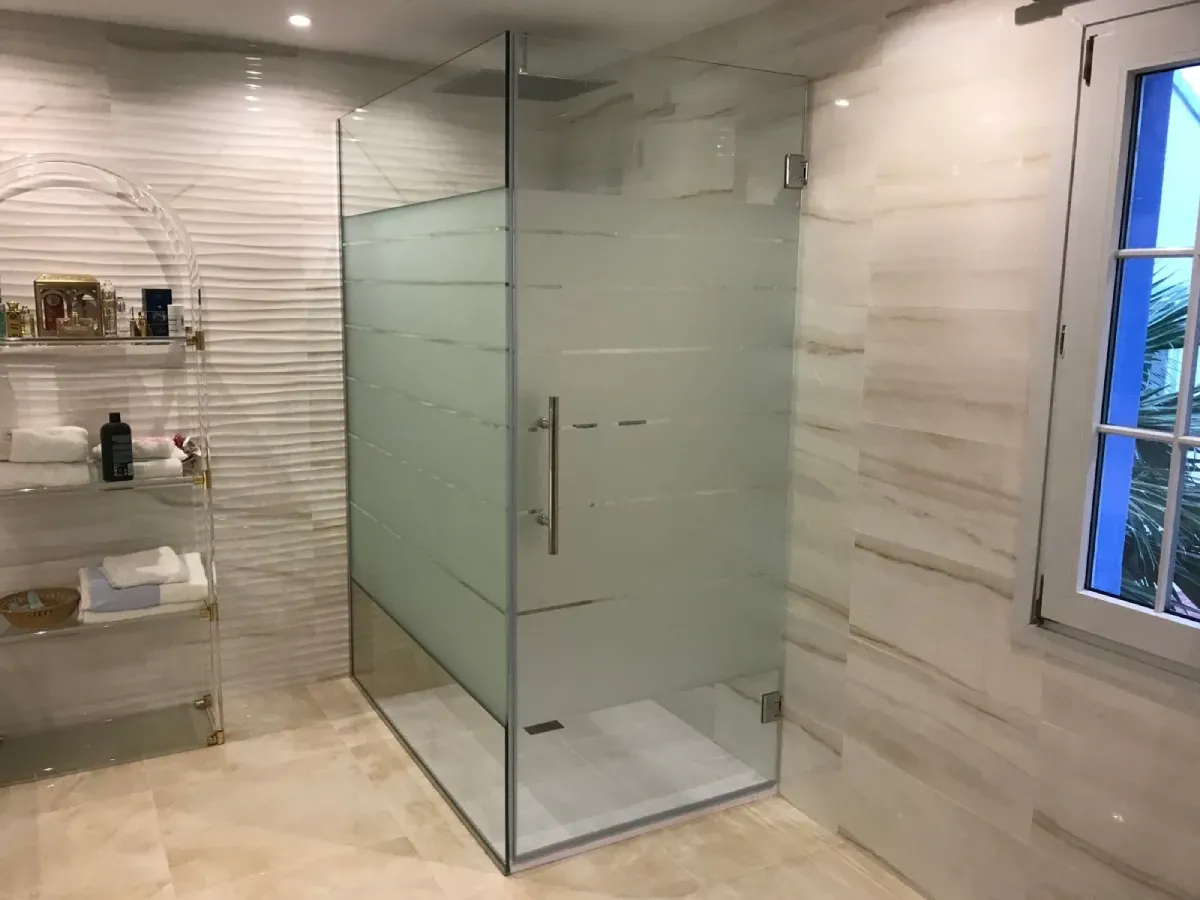 Una moderna cabina de ducha acristalada con cabezal de ducha tipo lluvia cromado, rociador de mano y paredes alicatadas.