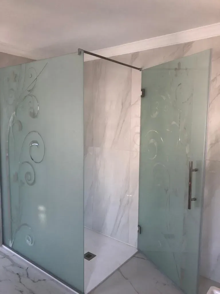 Una mampara de ducha de cristal con paneles de vidrio esmerilado con diseños de enredaderas grabados
