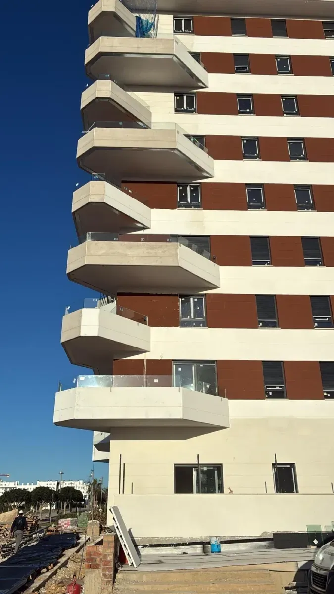 Vista exterior de un moderno edificio de apartamentos con balcones blancos apilados y sobresalientes.