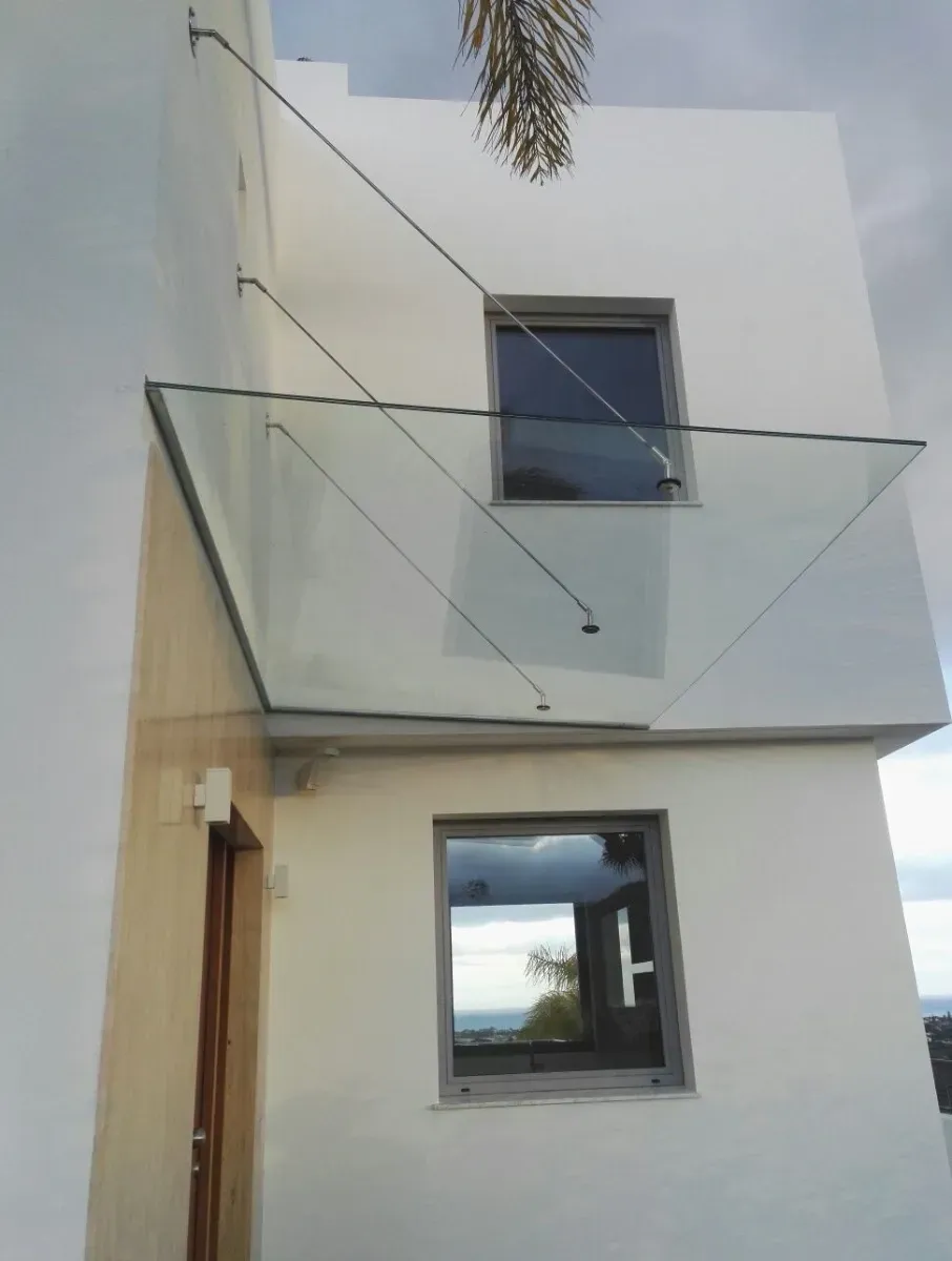 Un moderno edificio de fachada blanca con un toldo de cristal en voladizo sostenido por cables de tensión inclinados.