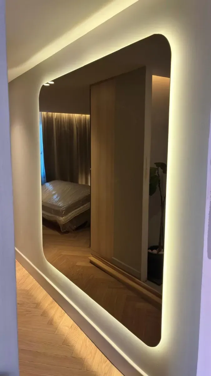 Un gran espejo de pared rectangular con esquinas redondeadas e iluminación LED cálida