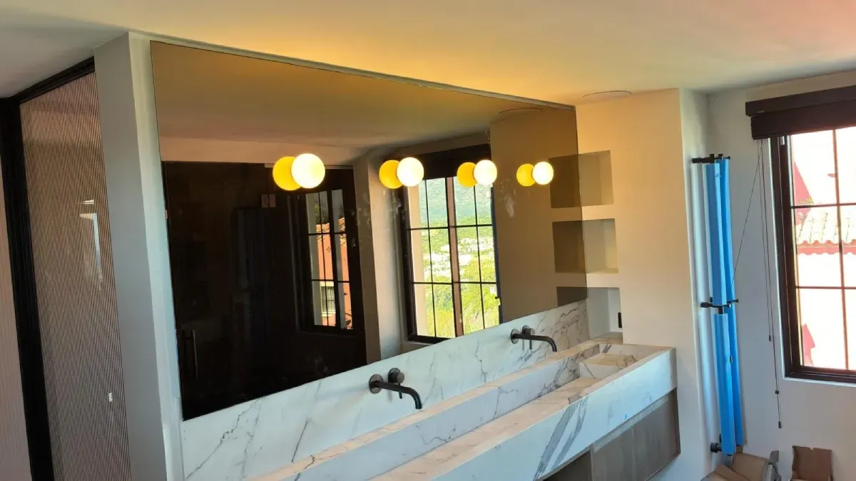 Un moderno mueble de baño con un gran espejo y cuatro lámparas esféricas montadas en la parte superior.