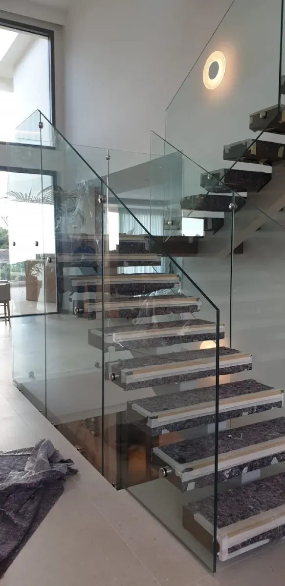 Una escalera con peldaños de madera modernos, barandillas de vidrio en un espacio interior luminoso y contemporáneo.