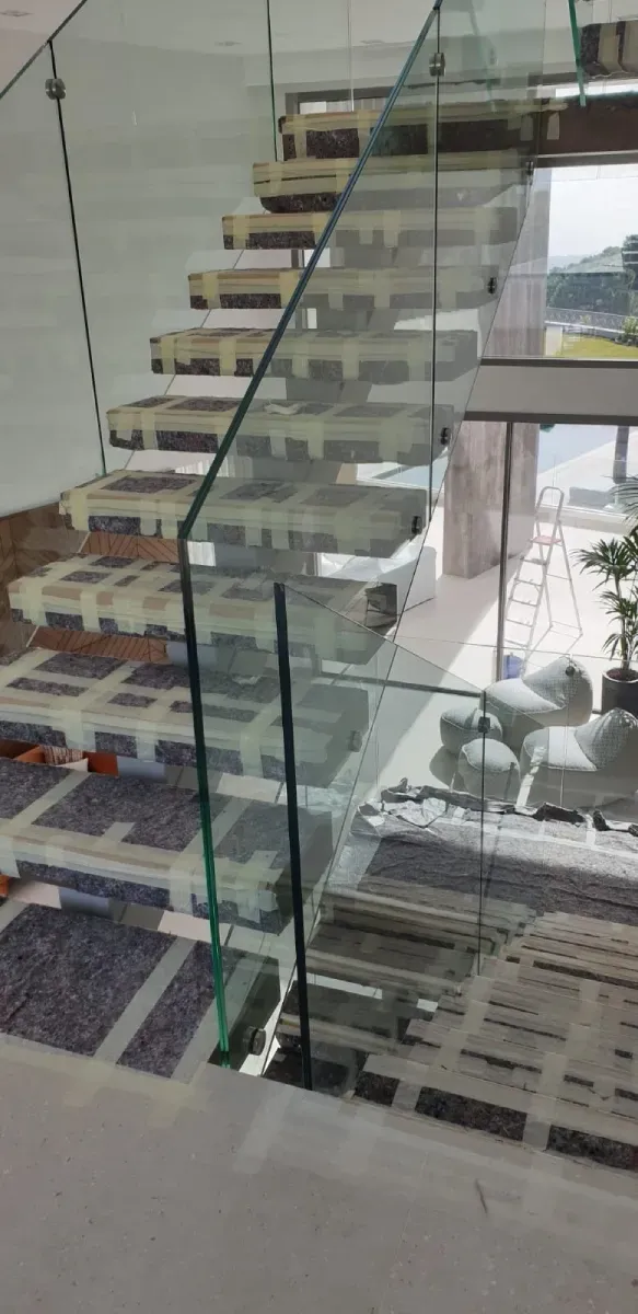 Una escalera en construcción cuenta con escalones de madera flotantes y una barandilla de vidrio transparente.