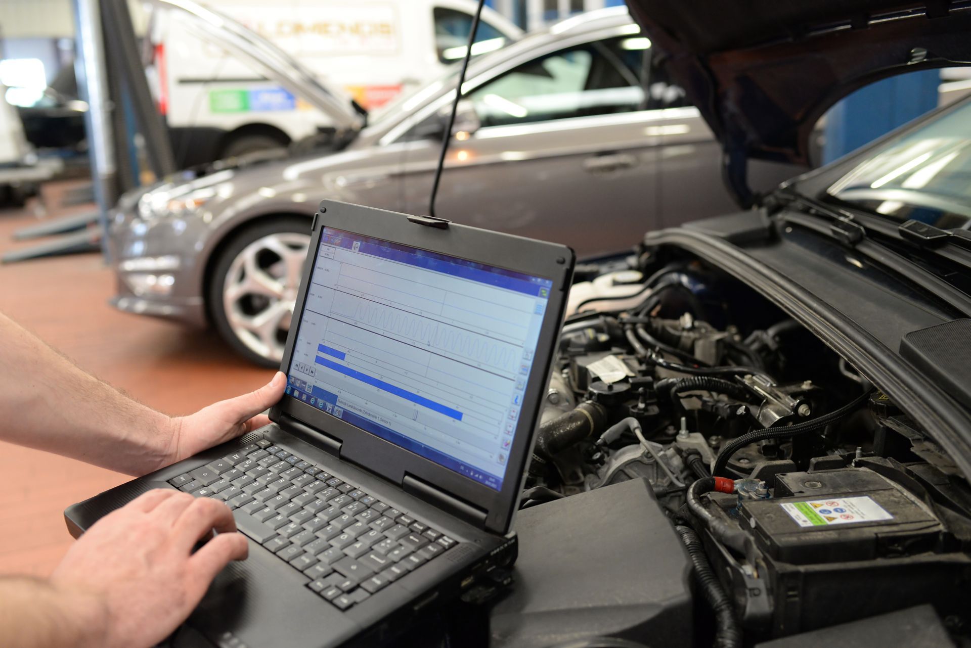 Un mécanicien utilise un ordinateur portable pour diagnostiquer le moteur d'une voiture, capot ouvert, dans un garage.