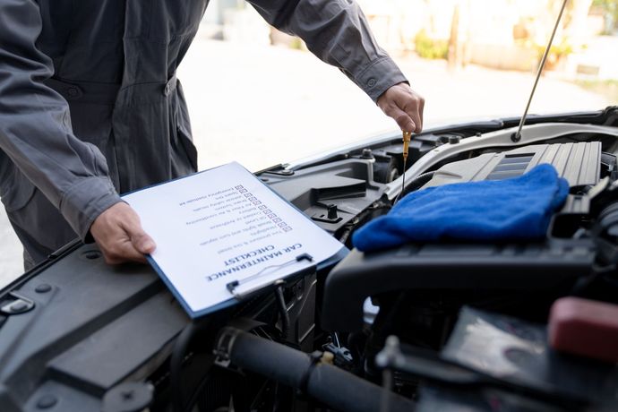 Un mécanicien vérifie le moteur d'une voiture à l'aide d'une liste de contrôle, en extérieur.