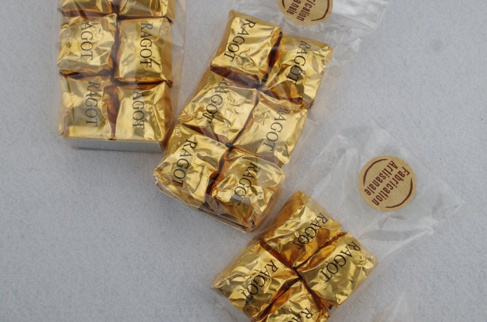 Chocolats emballés dans du papier doré, disposés en groupes dans des sachets en plastique transparent, sur une surface blanche.