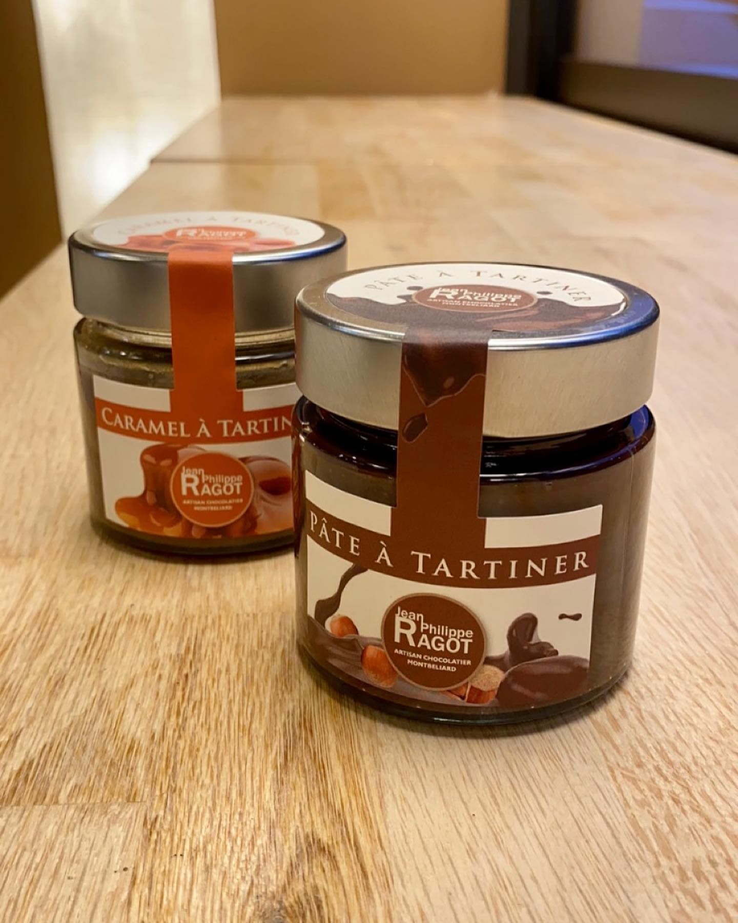 Deux pots en verre de pâte à tartiner, Caramel et Chocolat, sur une surface en bois.