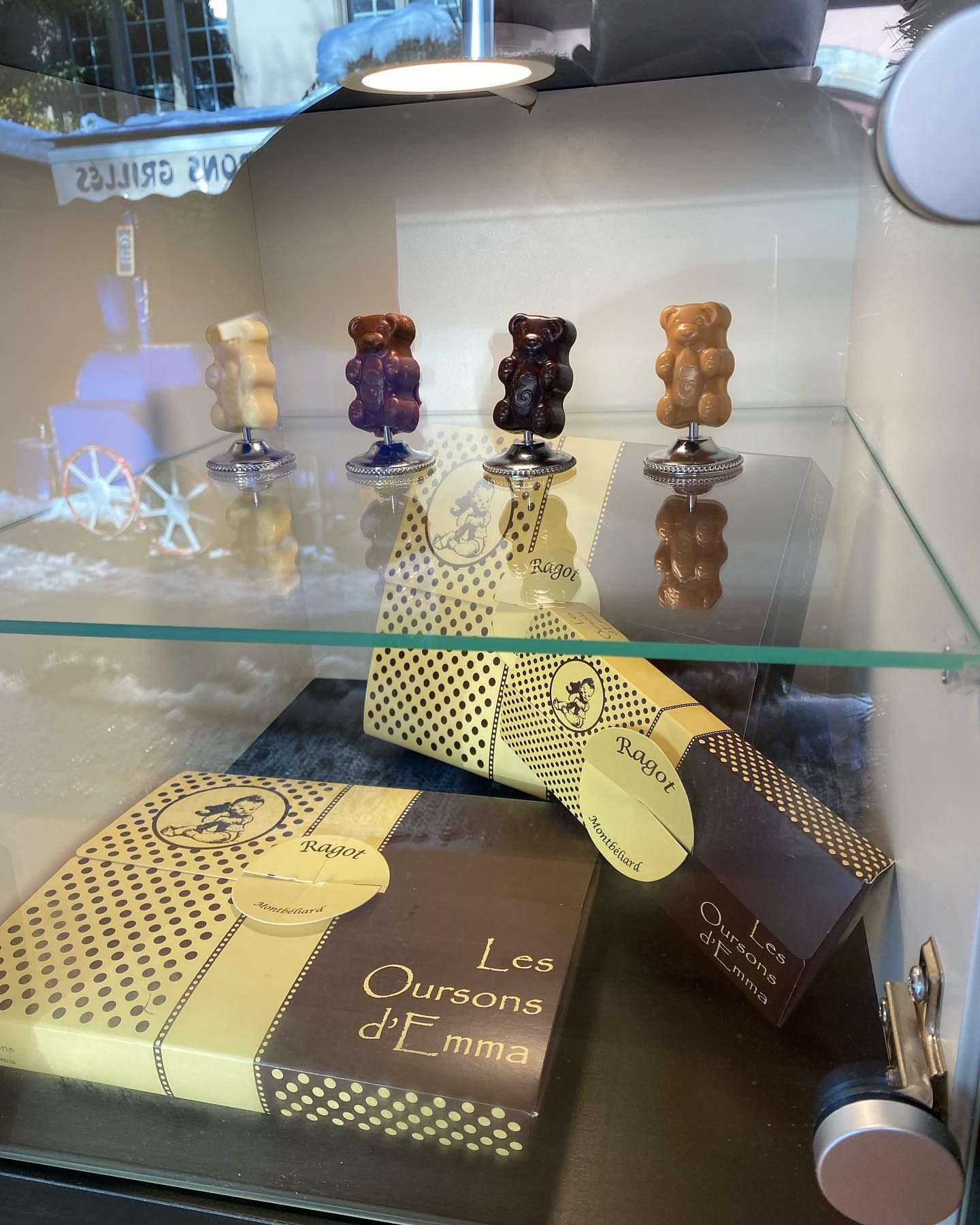 Sculptures d'oursons en gélatine au chocolat présentées dans une vitrine en verre, avec des coffrets cadeaux en dessous.