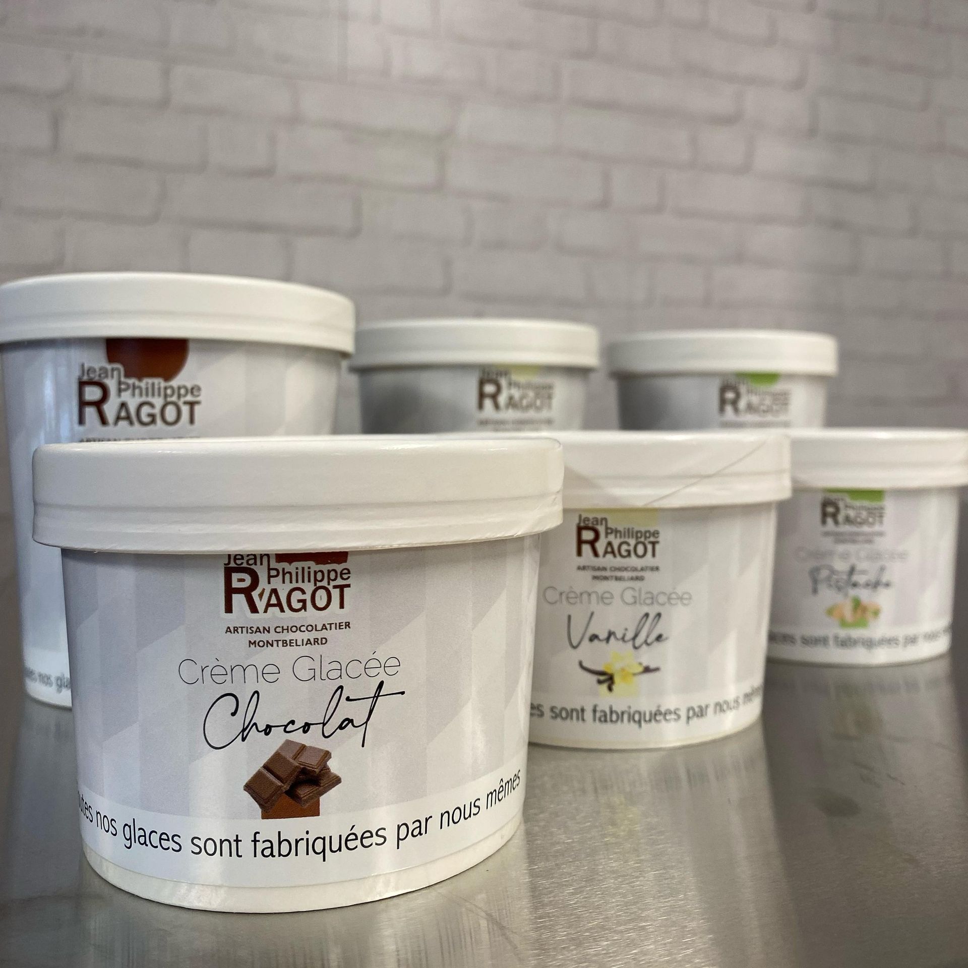 Plusieurs pots de glace étiquetés Jean-Philippe Ragot avec différents parfums comme le chocolat et la vanille.