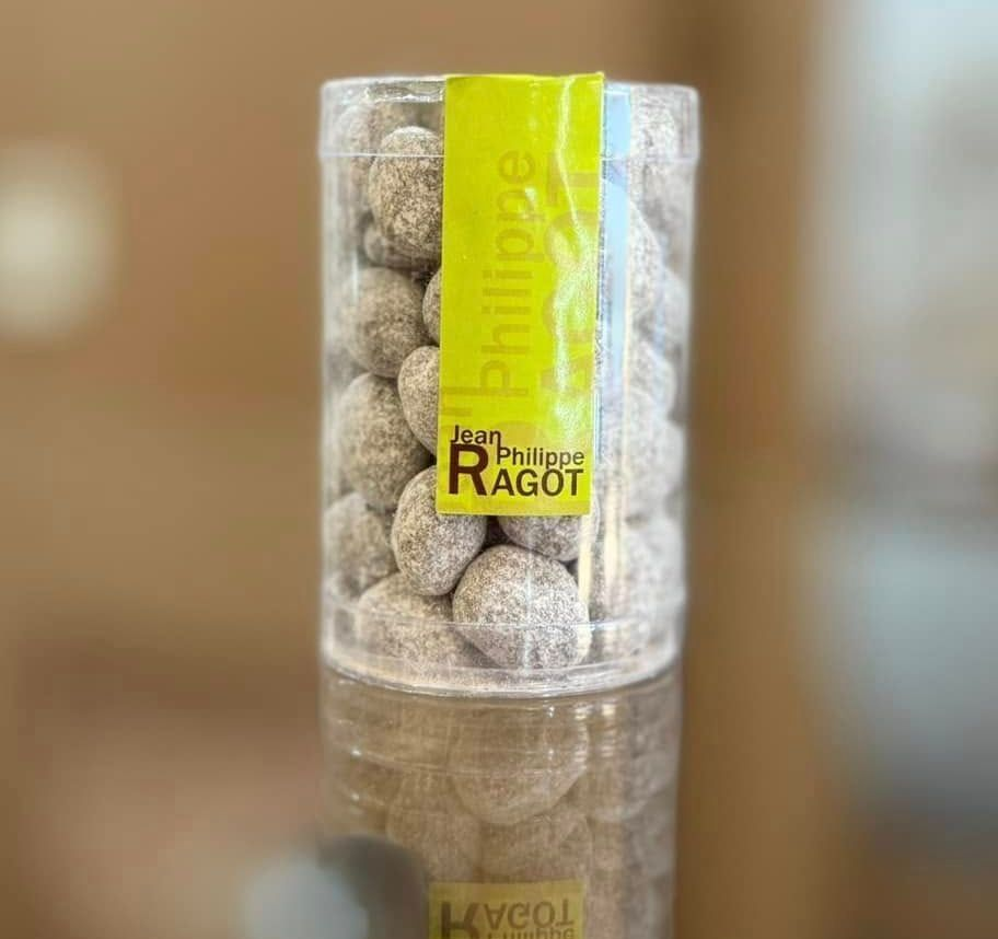 Un cylindre en plastique transparent de bonbons au chocolat, étiqueté Jean-Philippe RAGOT devant un arrière-plan flou.