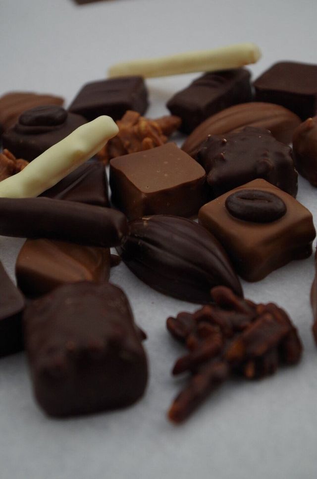 Assortiment de chocolats noirs, au lait et blancs sur une surface blanche. Formes et textures variées.