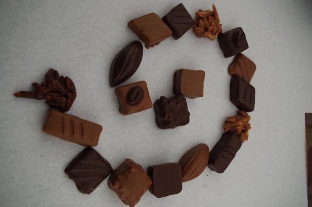 Disposition en spirale de chocolats assortis sur une surface blanche, comprenant des friandises de couleur noire, au lait et caramel.