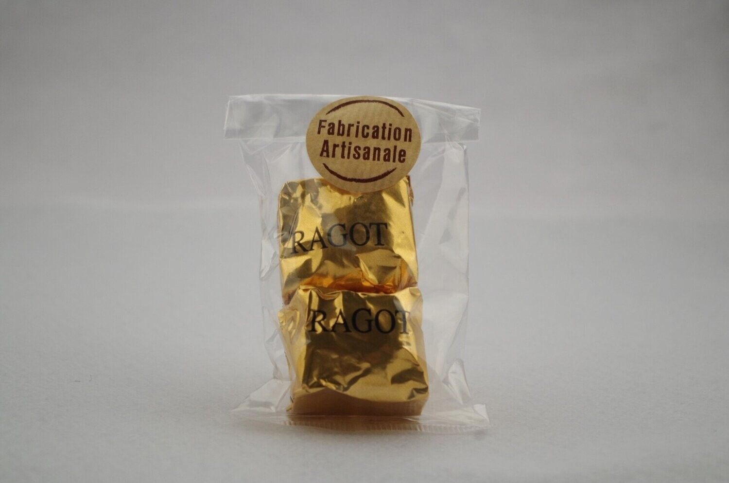 Deux bonbons emballés dans un paquet doré à l'intérieur d'un sac transparent, scellé avec un autocollant Fabrication Artisanale.