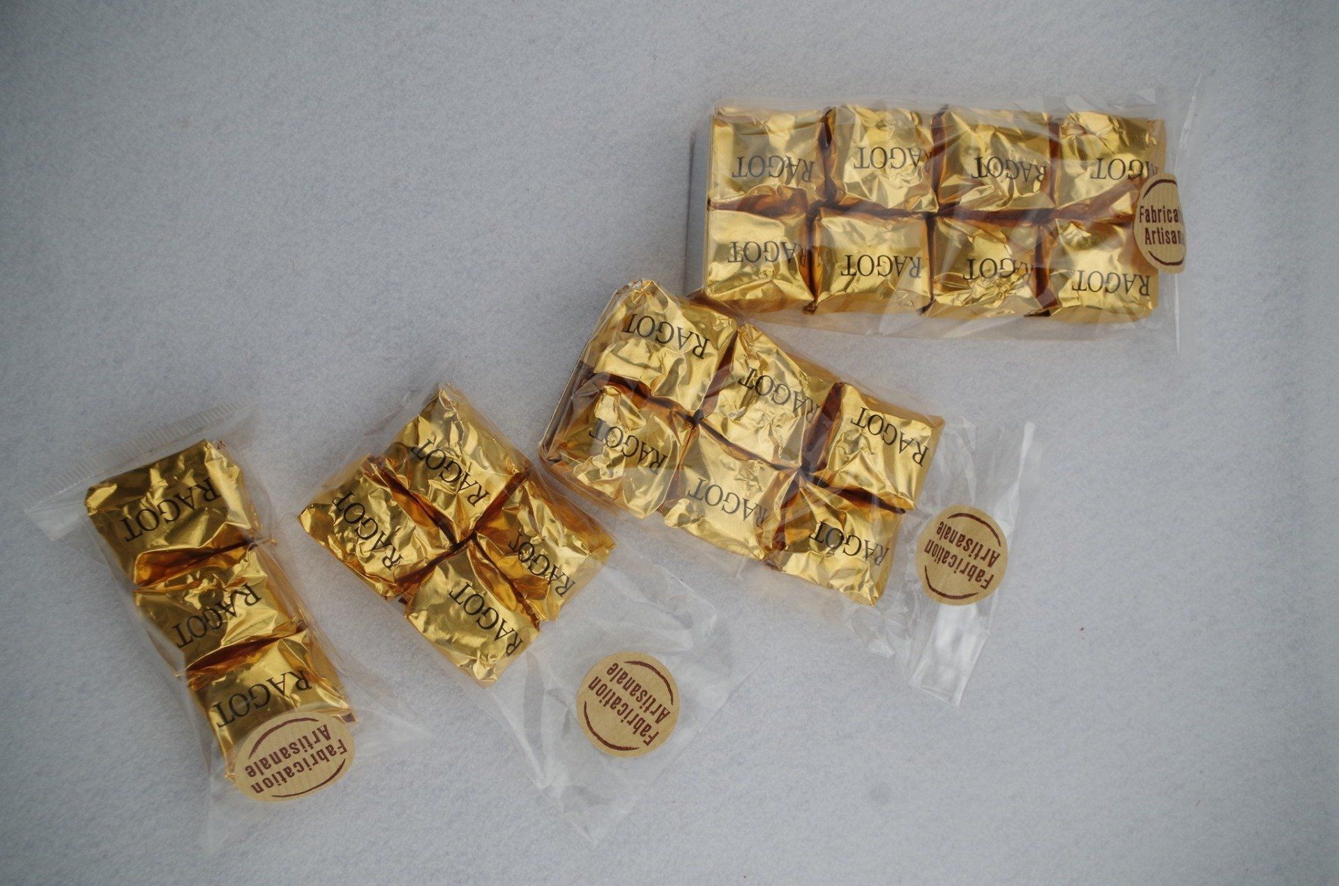 Chocolats emballés dans du papier doré, disposés en groupes dans des sachets en plastique transparent, sur une surface blanche.