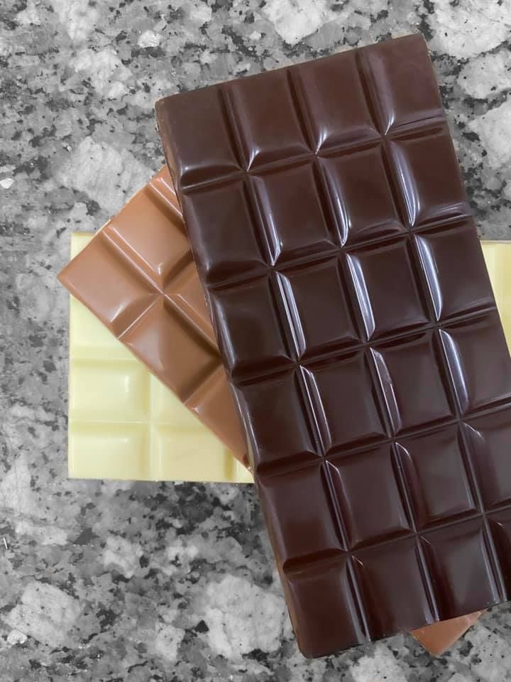 Trois barres de chocolat, chocolat noir, chocolat au lait et chocolat blanc, empilées sur une surface en marbre.