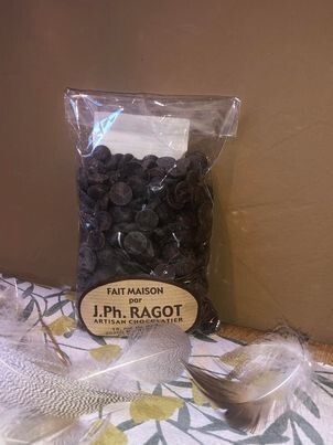 Sachet de pépites de chocolat noir, avec l'étiquette J.Ph. Ragot, présenté sur un tissu à motifs de plumes.