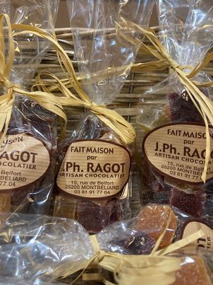 Gros plan sur des bonbons artisanaux emballés, attachés avec du raphia, étiquetés J.Ph. Ragot, Artisan Chocolatier.