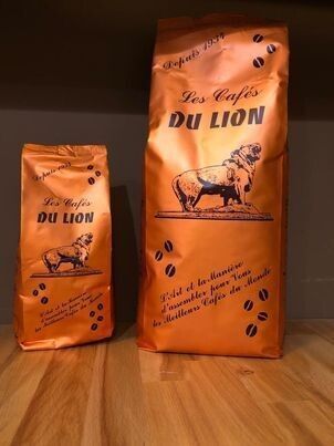 Deux sacs orange de café Les Cafés Du Lion avec le logo d'un lion, sur une surface en bois.