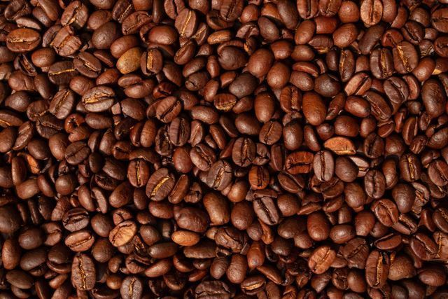 Grains de café torréfiés, bruns avec de subtiles variations de tons, remplissant le cadre.