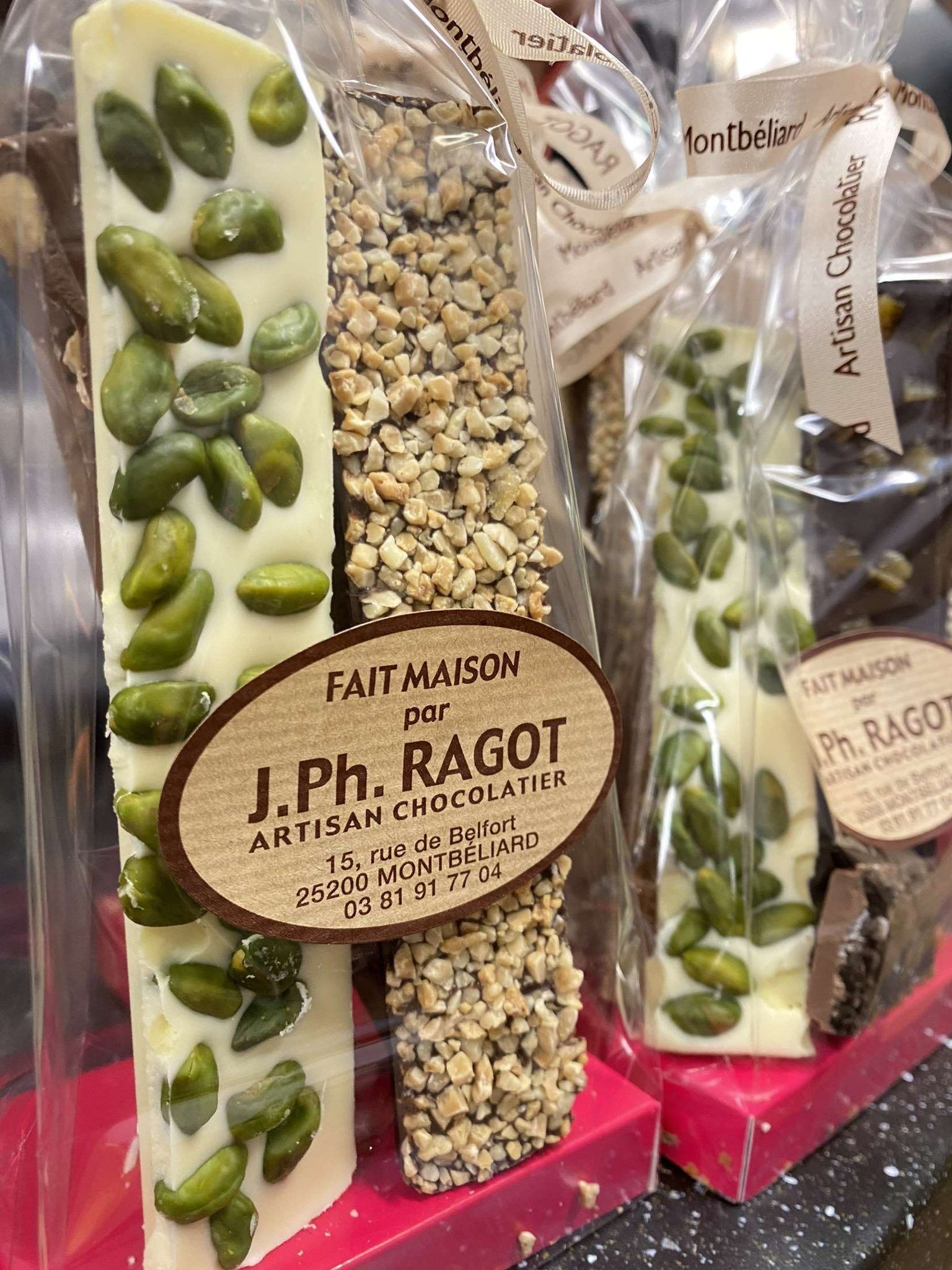 Gros plan sur des barres de chocolat emballées avec des pistaches et des noix, présentées dans un décor de magasin.