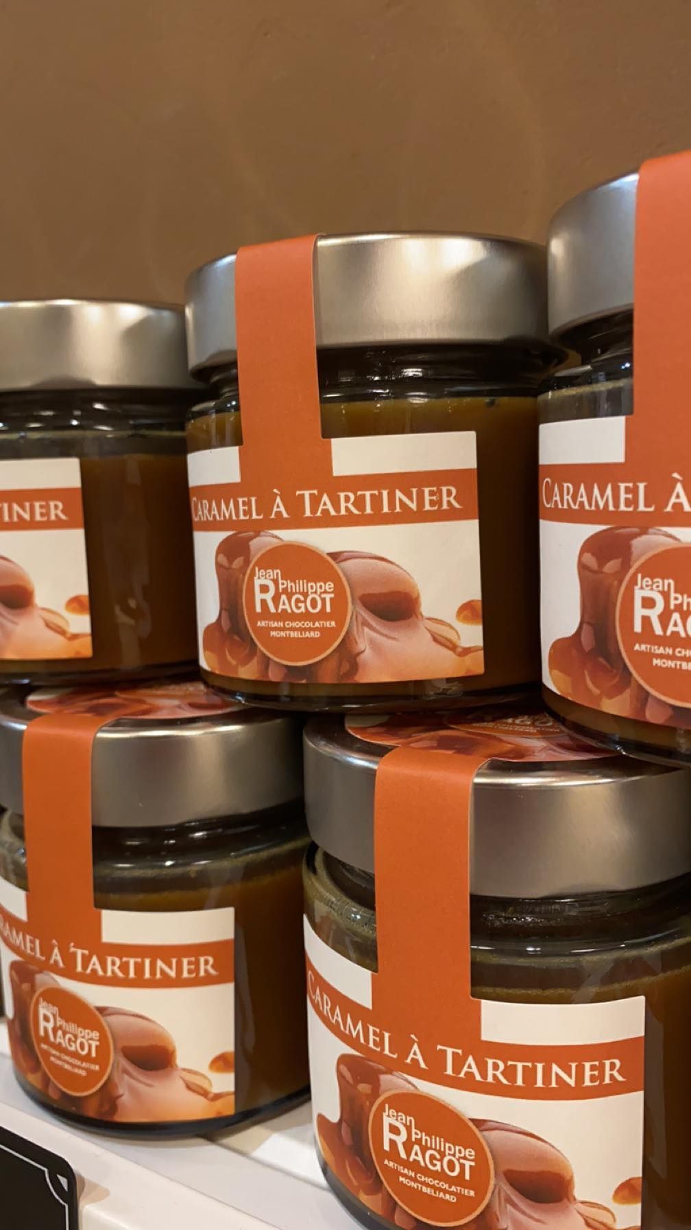 Des pots de pâte à tartiner au caramel empilés sur une étagère ; chacun porte une étiquette orange.