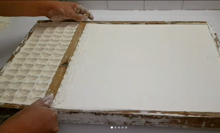 Des mains lissent la pâte sur une planche ; de petites formes de nouilles carrées à gauche.