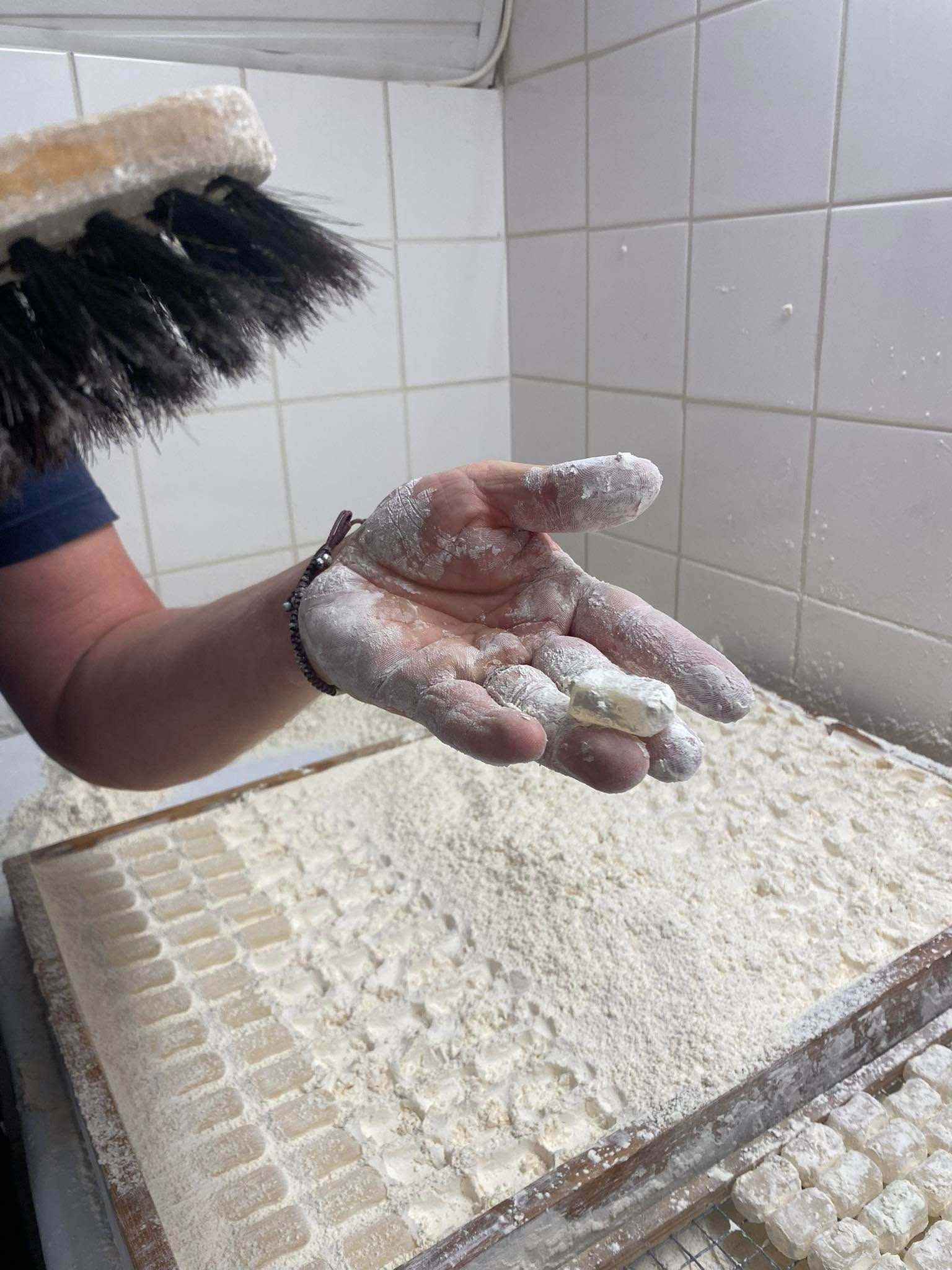 Une personne saupoudrant une main de poudre blanche sur un plateau de blocs saupoudrés de blanc dans une cuisine.