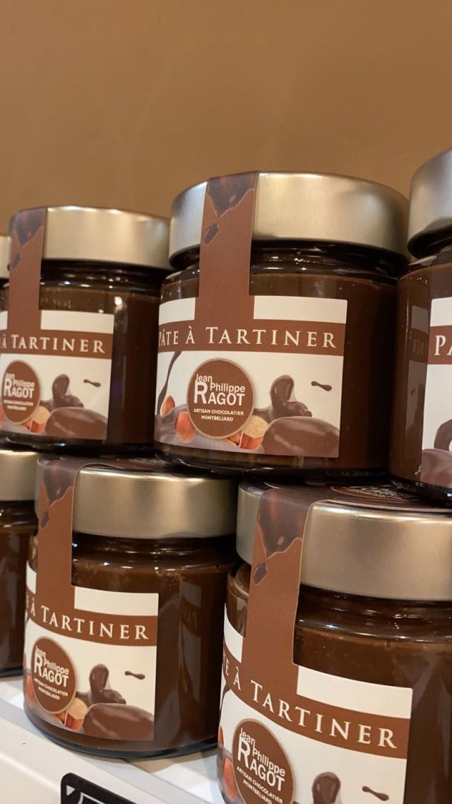 Pots de pâte à tartiner aux noisettes avec des étiquettes brunes, empilés sur une étagère, devant un fond marron.