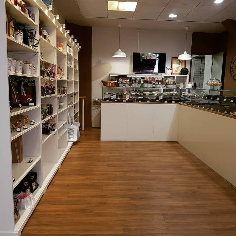 À l’intérieur d'une boutique lumineuse : étagères blanches avec produits, parquet, comptoir d'exposition avec desserts.