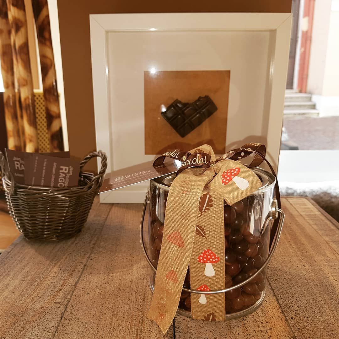 Coffret cadeau : contenant en verre plein de chocolats, ruban et décoration en forme de cœur encadrée sur une surface en bois.